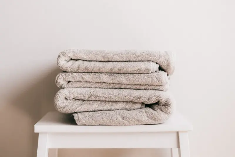 A neat stack of freshly folded towels on a stool against a plain wall